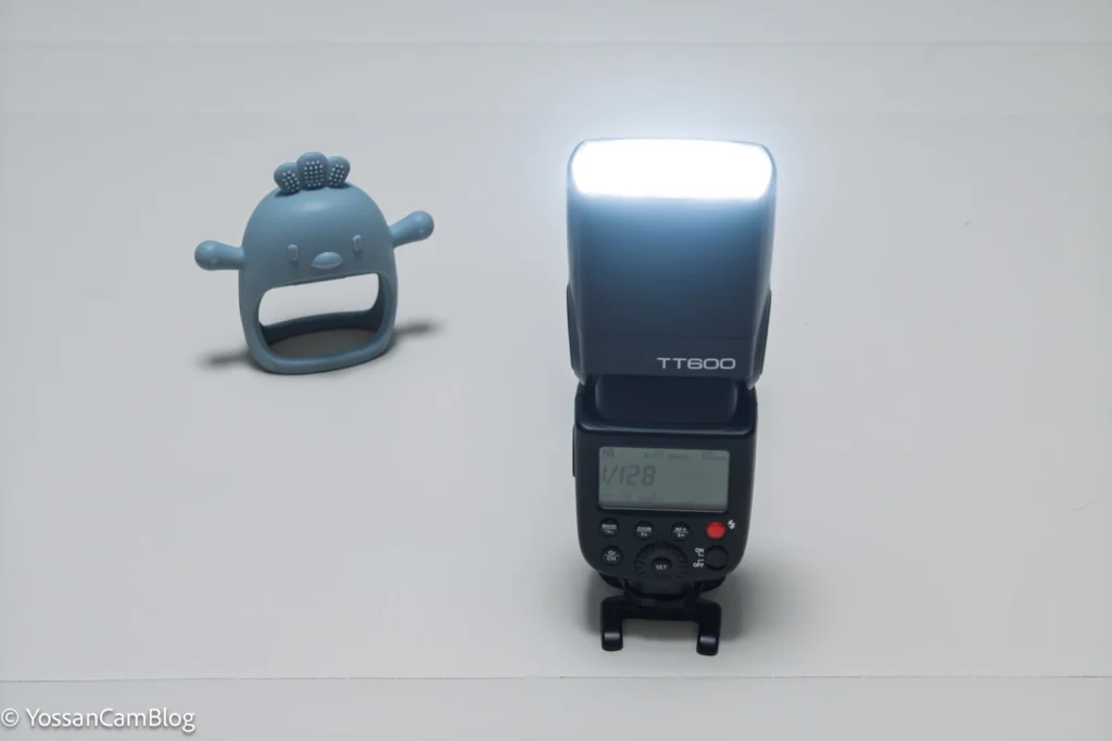 発光量1/128に設定したGodox TT600がヘッドを上に向けて光っている様子と、奥に置いた歯固めのおもちゃ