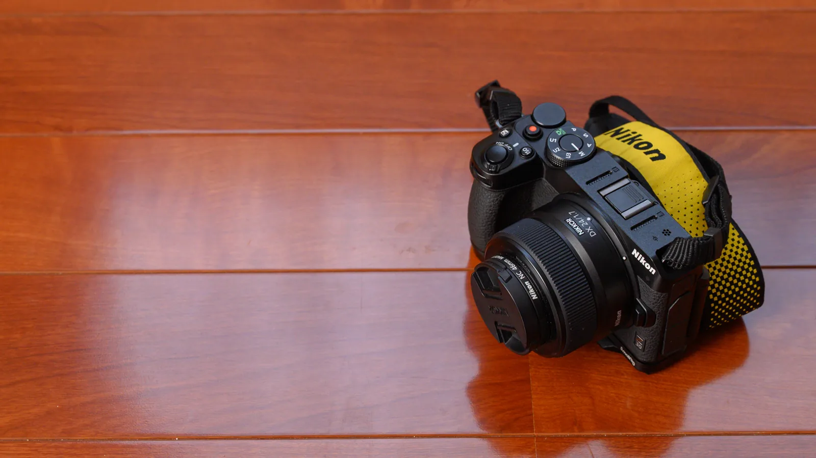 木目の床に置いたNikon Z30に、NIKKOR Z DX 24mm f/1.7を付けたところ。黄色いニコンのストラップが付いている