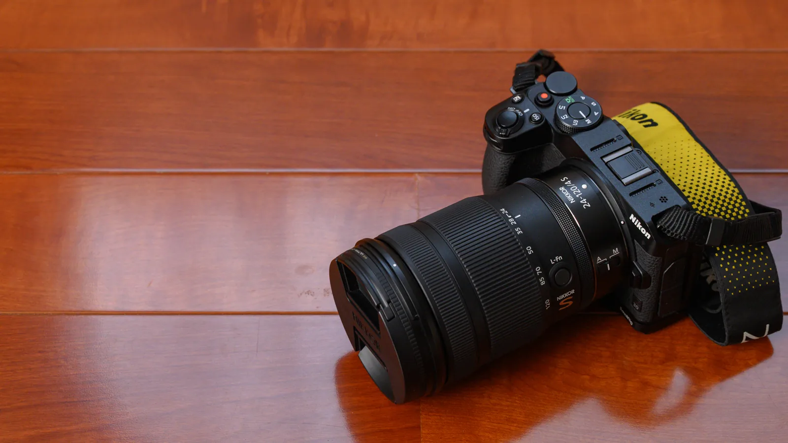 木目の床に置いたNikon Z30に、NIKKOR Z 24-120mm f/4 Sを付けたところ。レンズキャップが付いている